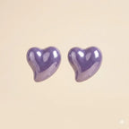 Pair of glossy purple puffy heart stud earrings with high-shine lacquer finish on beige background