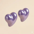 Pair of glossy purple puffy heart stud earrings with high-shine lacquer finish on beige background