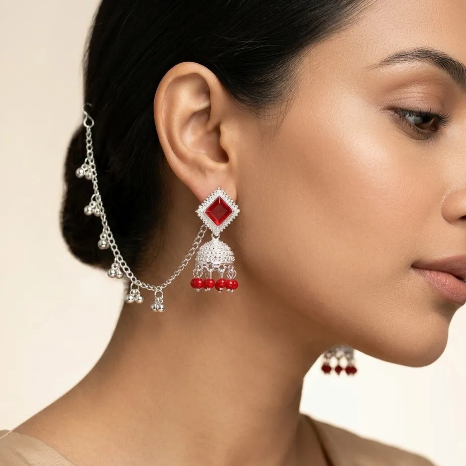 Woman wearing silver red stone jhumka earrings with ghungroo kan chain draped into hair on festive occasion
