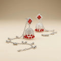 Close-up of silver diamond stud jhumka earrings with red bead drops and cascading silver ghungroo ball hair chain

