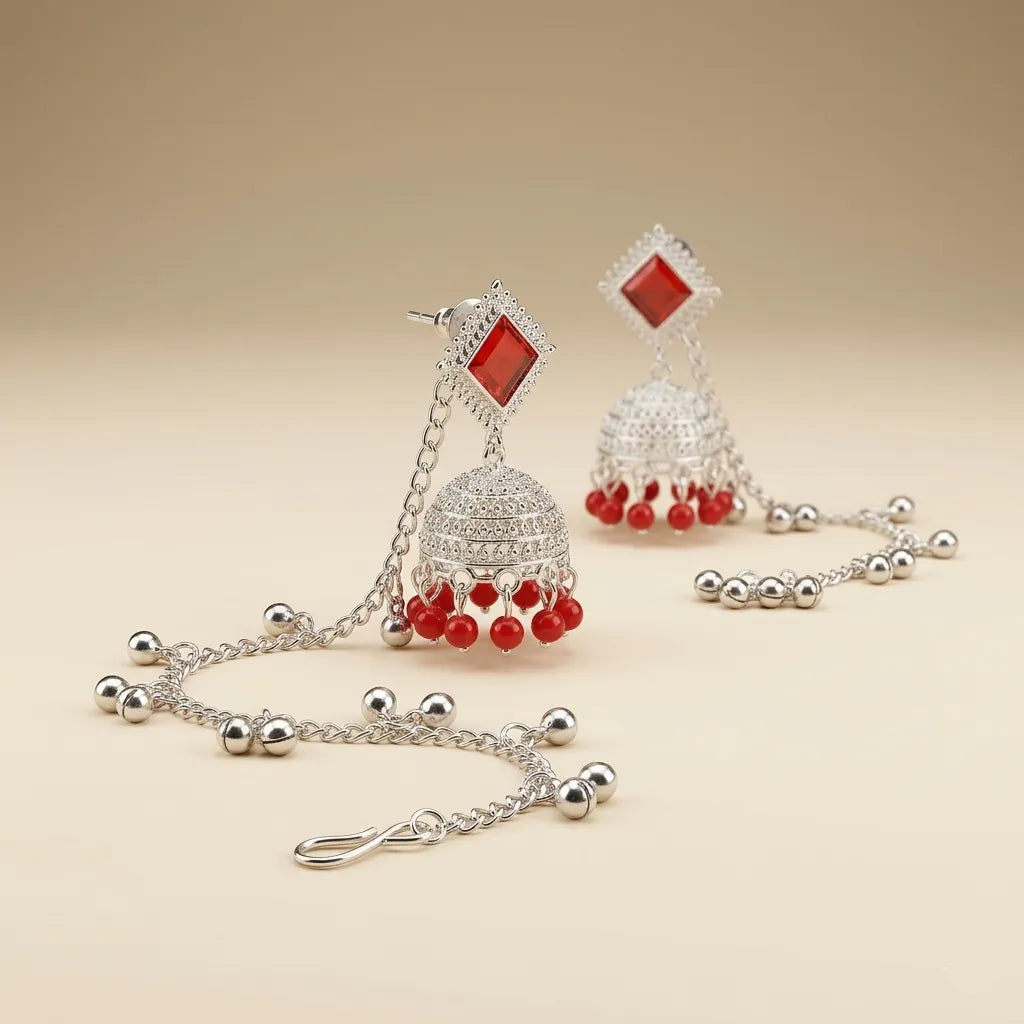 Close-up of silver diamond stud jhumka earrings with red bead drops and cascading silver ghungroo ball hair chain
