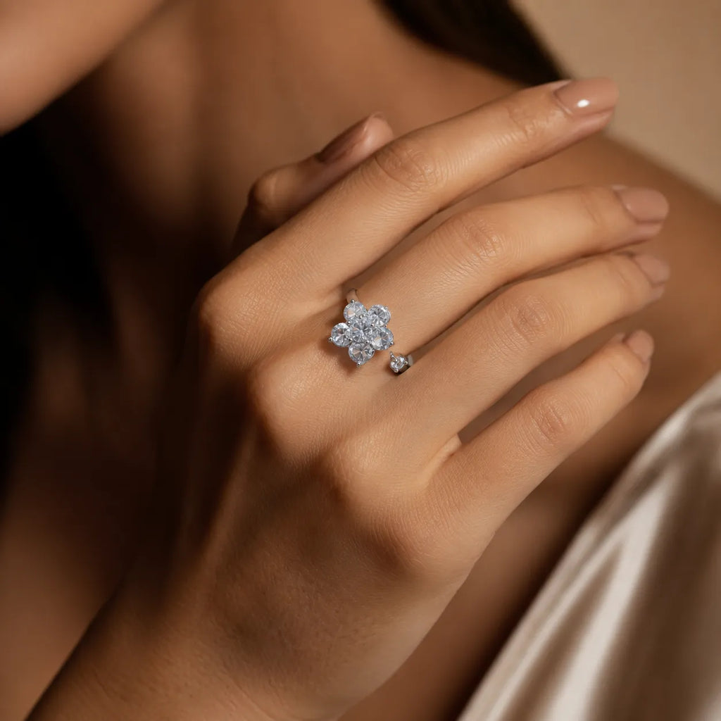 A close-up lifestyle shot of a woman's hand wearing a silver ring with a flower-shaped cluster of clear gemstones and a small matching stone on her other finger.
