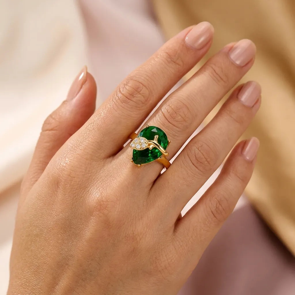 "Woman wearing emerald green pear-cut gold ring with vine leaf design on ring finger"