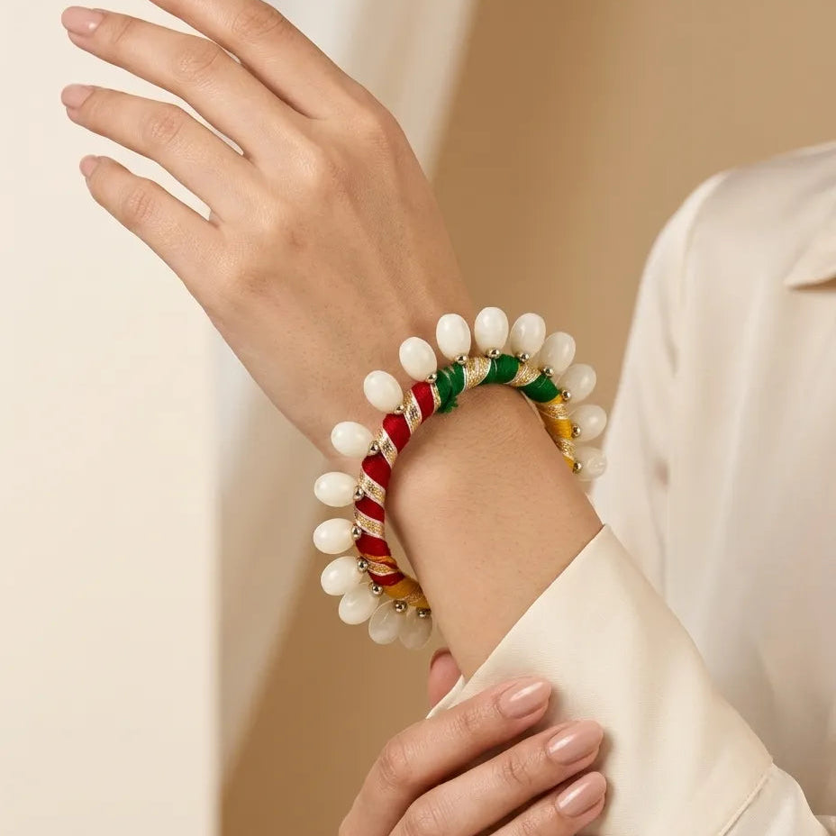 Woman wearing two stacked multicolor silk thread bangles with white shell drop fringe on wrist with cream outfit