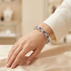 Woman wearing silver deep purple amethyst CZ halo bangle bracelet on wrist with white outfit resting on cream satin