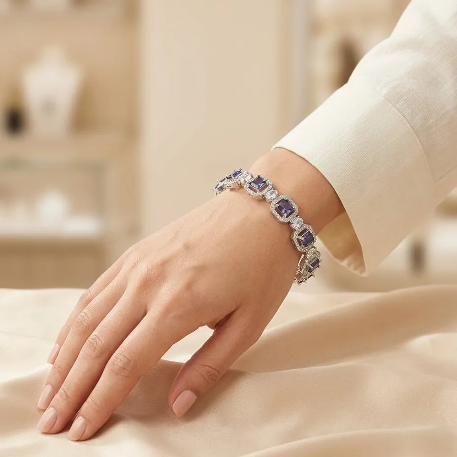 Woman wearing silver deep purple amethyst CZ halo bangle bracelet on wrist with white outfit resting on cream satin