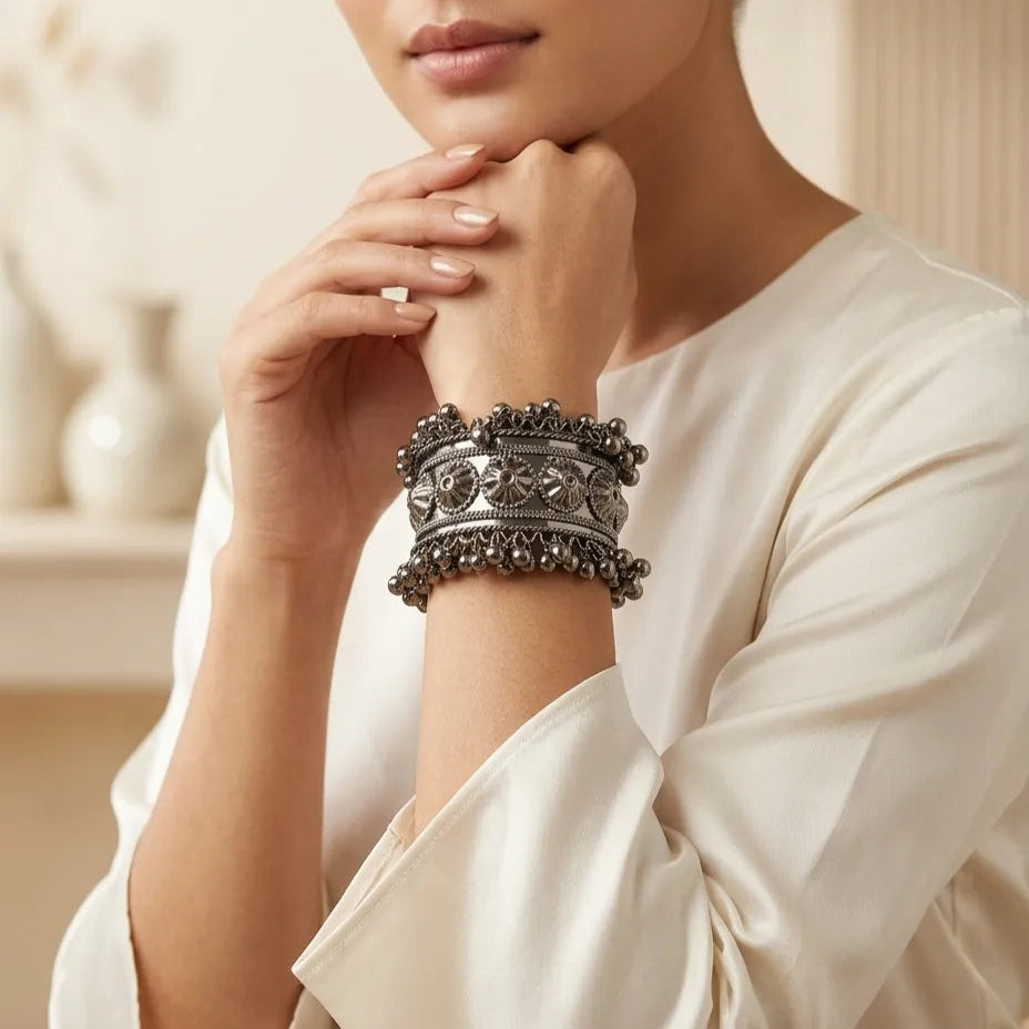 Woman wearing oxidized silver floral embossed wide cuff bangle with ghungroo drops on wrist styled with white ethnic outfit