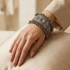 Close-up of woman's wrist wearing oxidized silver broad tribal cuff bangle with floral motifs and silver ball drops resting on cream fabric