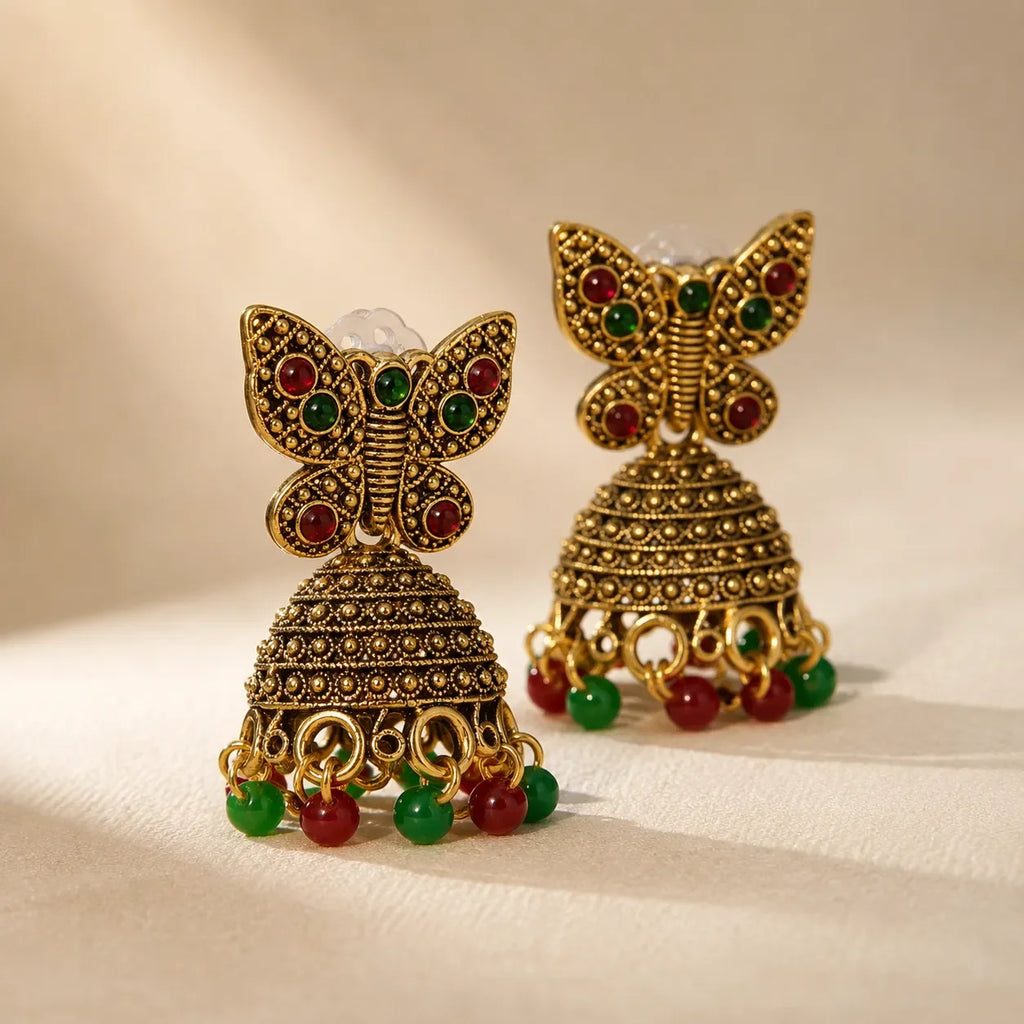 Close-up of antique gold butterfly jhumka earrings showing textured dome bell and alternating red green bead drops