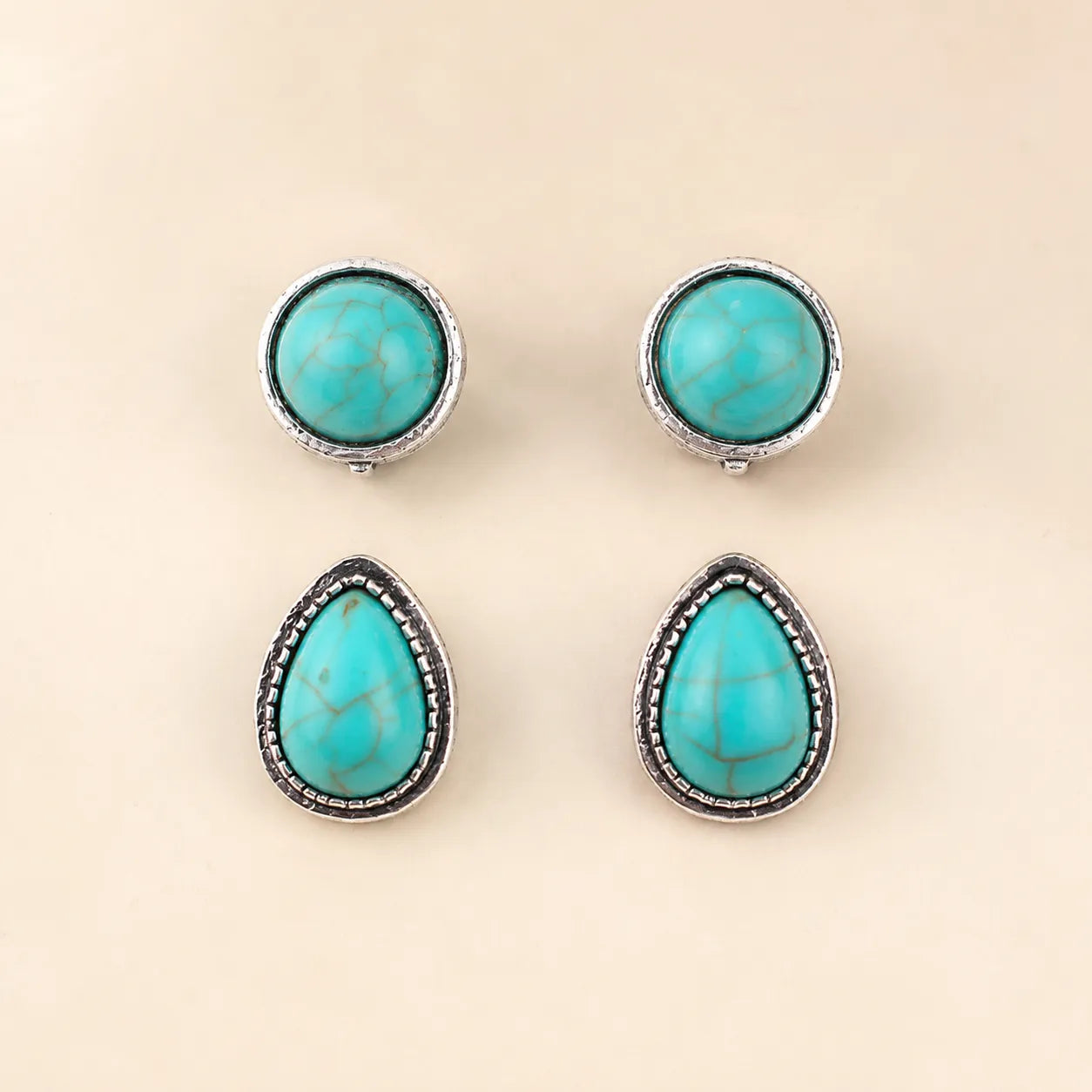 Flat lay of two turquoise earring pairs, round and teardrop shapes, antique silver trim