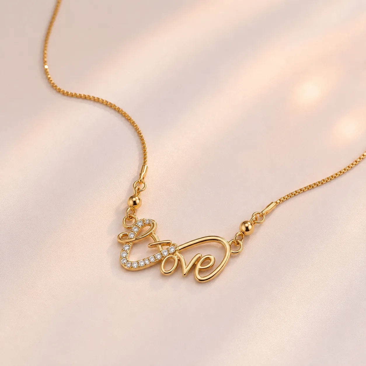 Gold plated cursive Love script necklace with CZ heart accent, laid flat on beige background