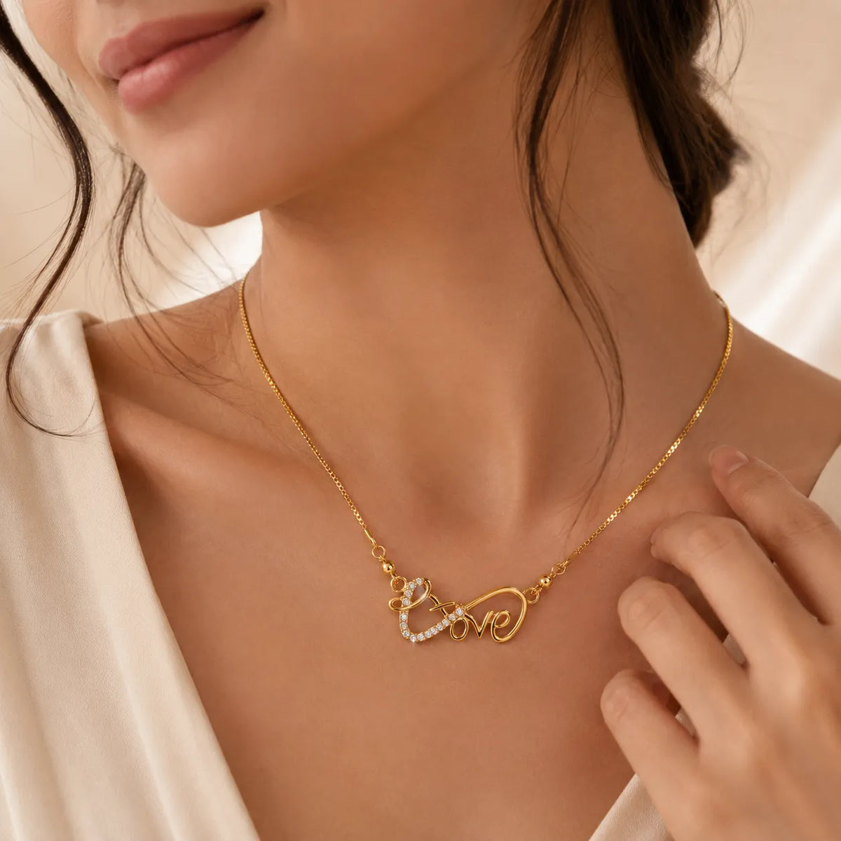 Woman wearing gold cursive Love necklace with crystal heart pendant, close-up on neckline