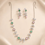 Silver crystal vine leaf necklace and matching drop earrings with pink and green flower accents, laid flat on beige background