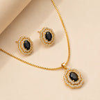 Close-up of gold vintage floral necklace and earring set with black gemstone centers on beige backdrop