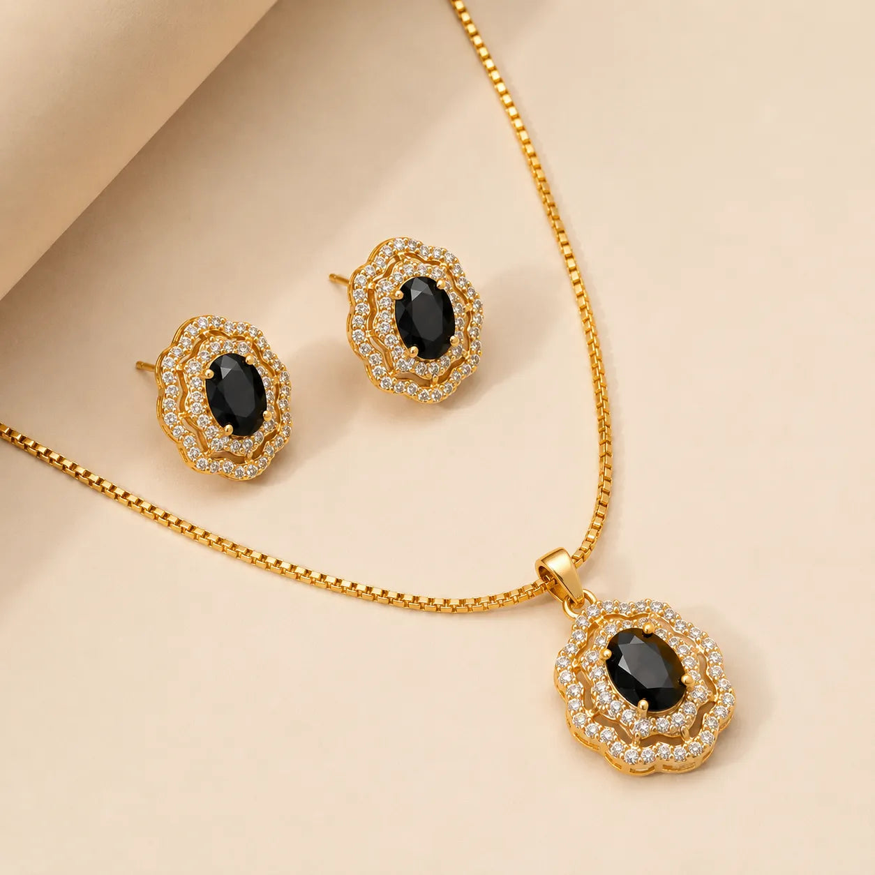 Close-up of gold vintage floral necklace and earring set with black gemstone centers on beige backdrop
