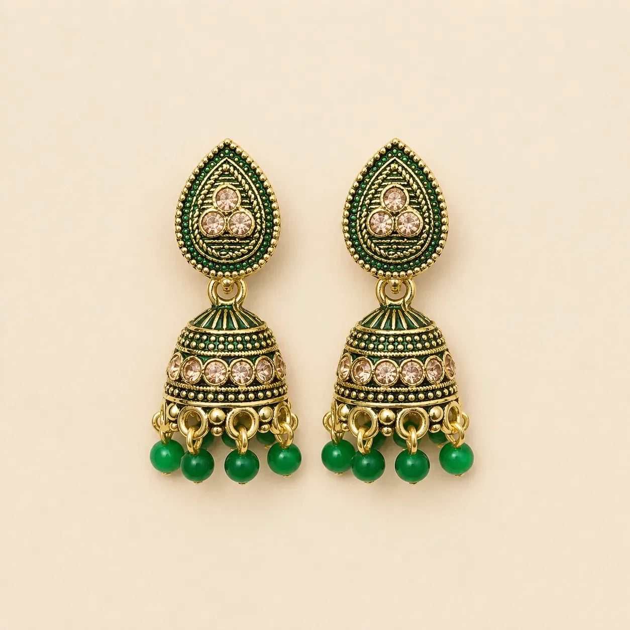 Pair of antique gold emerald green meenakari teardrop stud dome jhumka earrings with champagne crystal band and green bead drops on cream background