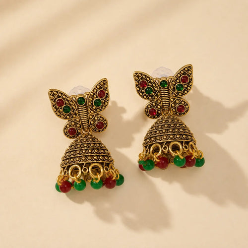 Antique gold butterfly jhumka earrings with red and green stone embellishments and bead drops on beige background