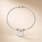 Silver open cuff ball-end bangle with white square smiley face enamel charm on cream background