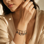 Woman wearing silver angel cherub and club suit charm bangle bracelet on wrist styled with cream satin outfit — Y2K celestial jewelry look