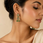 Woman wearing antique gold green meenakari teardrop jhumka earrings with emerald bead drops styled with cream satin outfit
