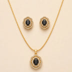 Gold plated necklace and stud earrings set with black onyx oval gemstones in vintage floral halo design, laid flat on beige background