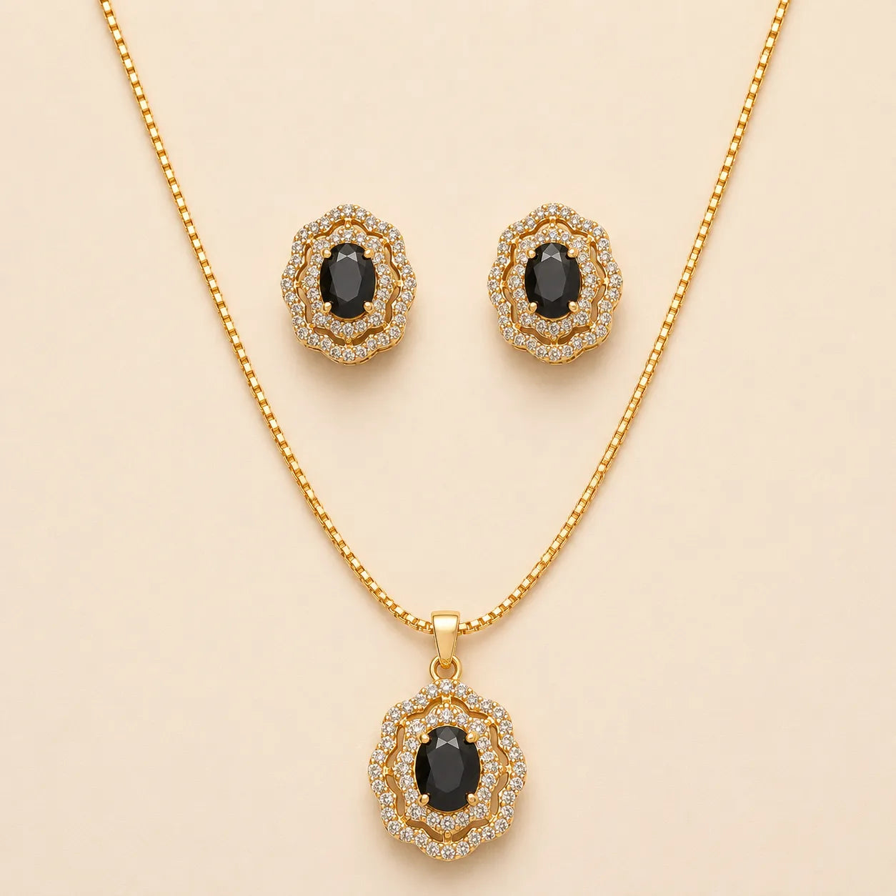 Gold plated necklace and stud earrings set with black onyx oval gemstones in vintage floral halo design, laid flat on beige background