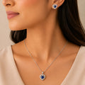 Woman wearing blue sapphire heart halo pendant necklace and matching stud earrings, close-up on neckline and ear