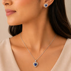 Woman wearing blue sapphire heart halo pendant necklace and matching stud earrings, close-up on neckline and ear