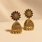 Pair of antique gold Navratna sunflower floral stud jhumka earrings with ruby emerald petals champagne crystal dome and pearl drops on cream background