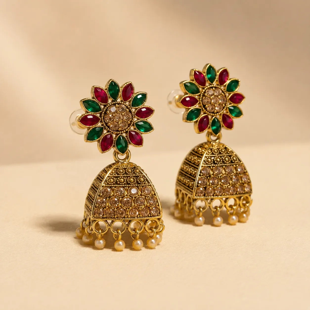 Pair of antique gold Navratna sunflower floral stud jhumka earrings with ruby emerald petals champagne crystal dome and pearl drops on cream background