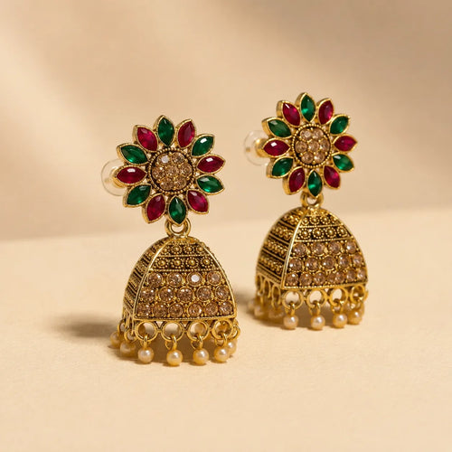 Pair of antique gold Navratna sunflower floral stud jhumka earrings with ruby emerald petals champagne crystal dome and pearl drops on cream background