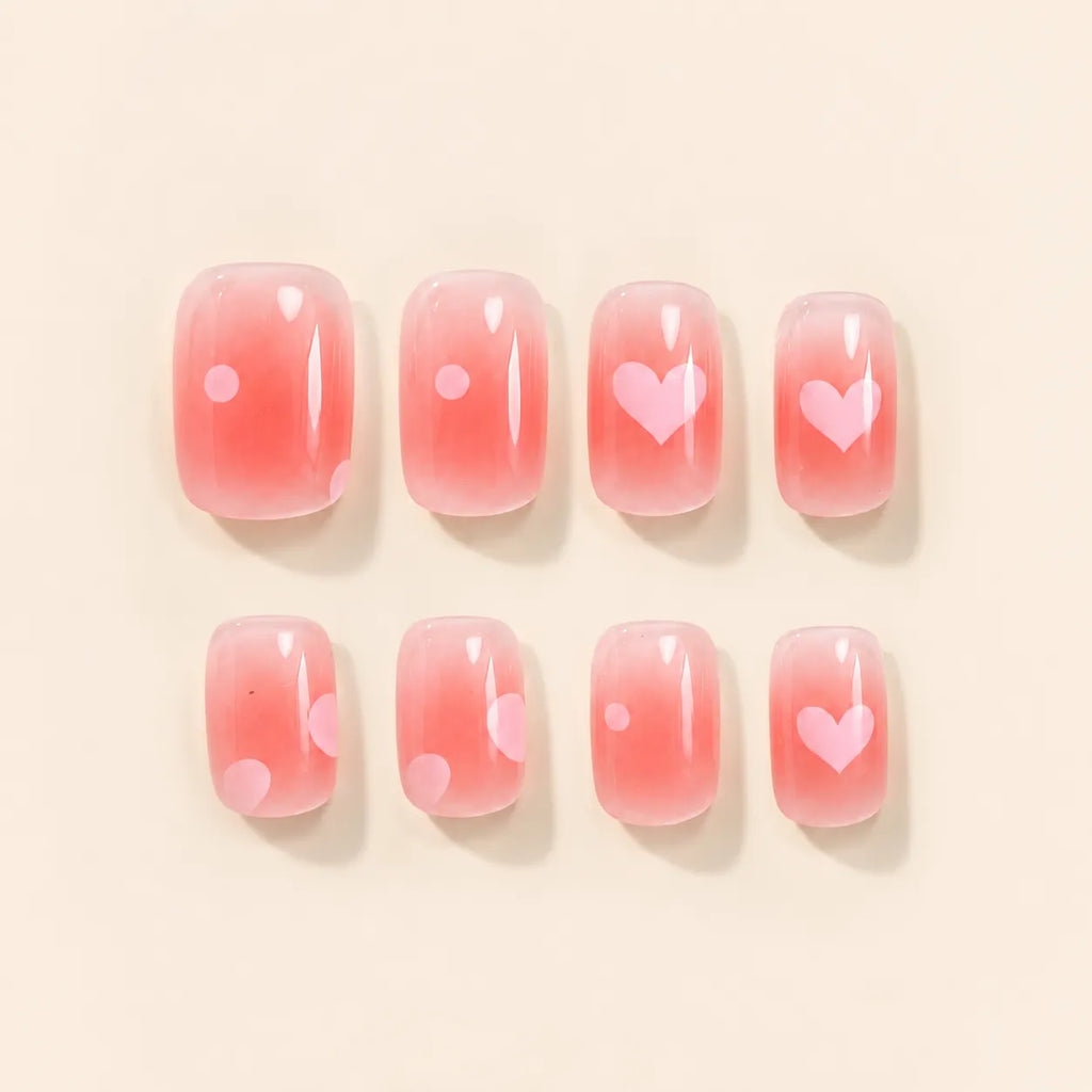 Eight pink ombre press on nails with pink heart and polka dot accents laid flat on beige background