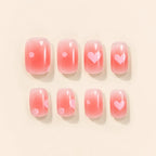 Eight pink ombre press on nails with pink heart and polka dot accents laid flat on beige background