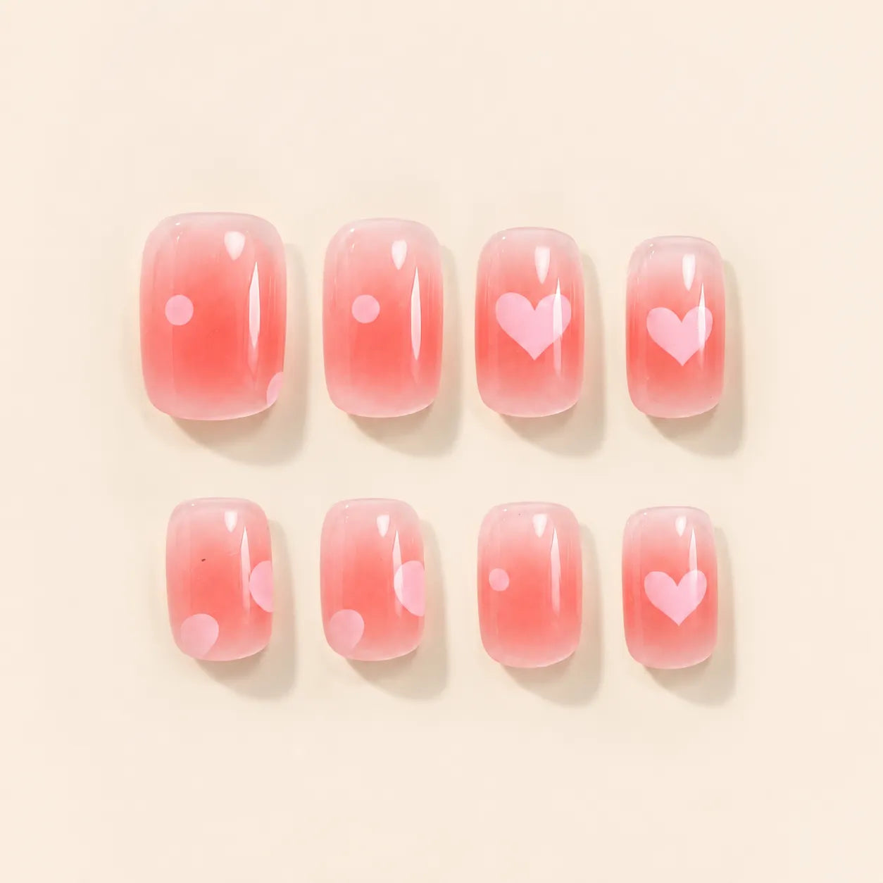 Eight pink ombre press on nails with pink heart and polka dot accents laid flat on beige background