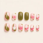 Twelve press on nails with sage green solid color and pink floral daisy accents laid flat on beige background