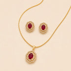 Gold jewelry set featuring a pendant necklace, matching stud earrings, and a chain, each with an oval deep red gemstone surrounded by a halo of small clear stones, displayed on a light beige background.