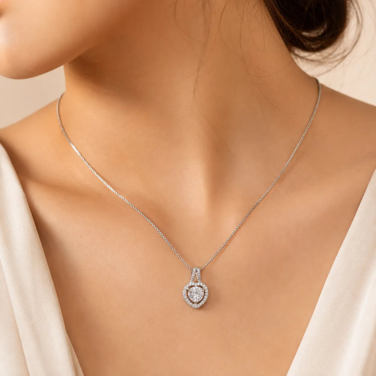 A close-up of a model wearing a delicate silver chain necklace with a heart-shaped pendant set with sparkling clear stones.