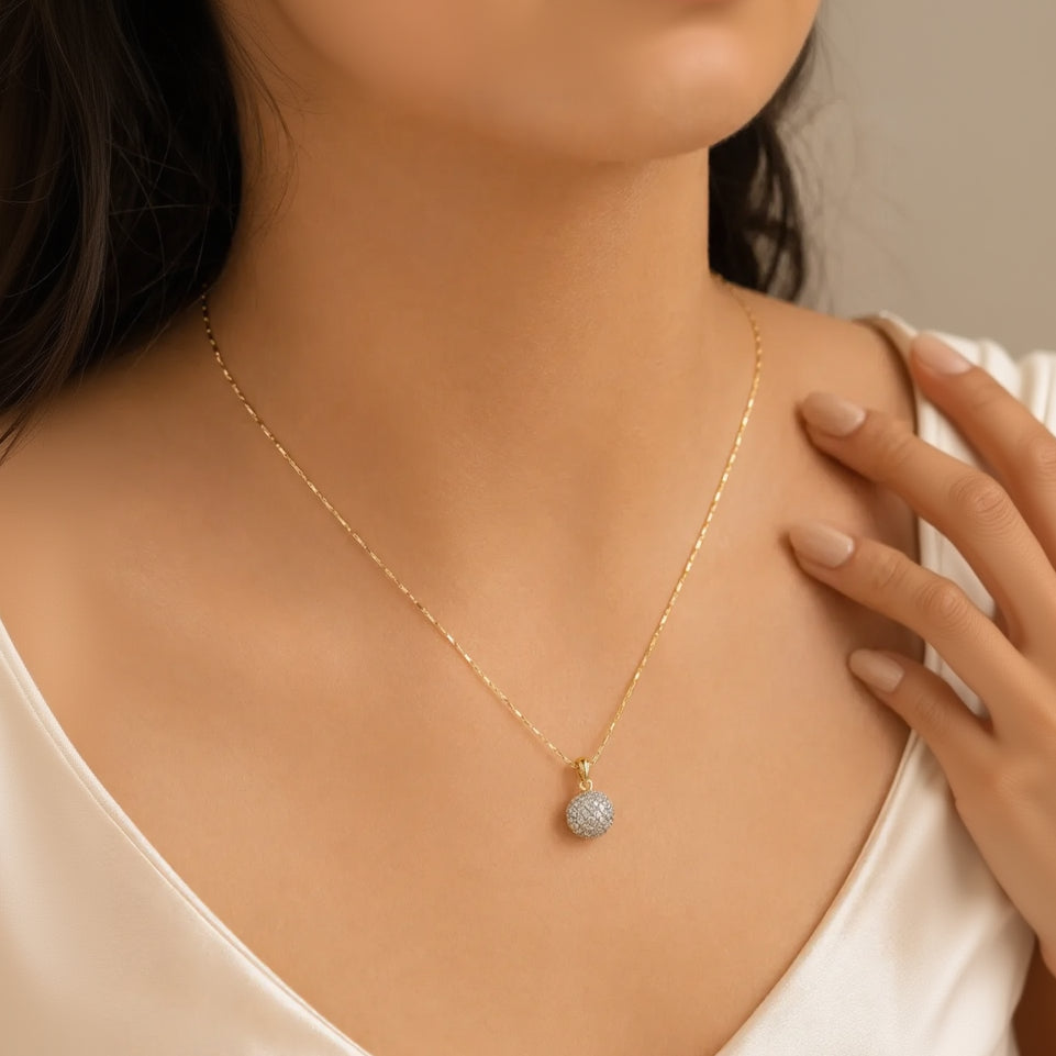 Woman wearing gold pavé crystal ball pendant necklace, close-up on neckline and collarbone