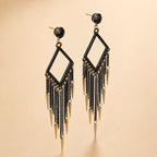Black tassel fringe earrings with gold spike drops and black crystal top, angled product photo on beige background