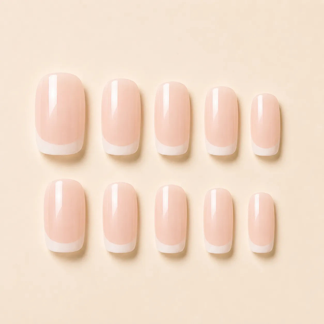  Ten French tip press on nails with nude pink base and white tips laid flat on beige background