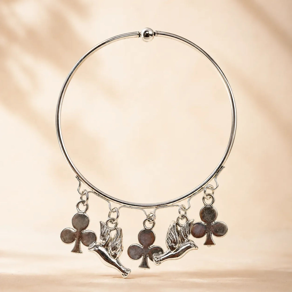Side angle view of silver angel cherub and club charm bangle bracelet showing charm detail and ball bead top closure on warm background