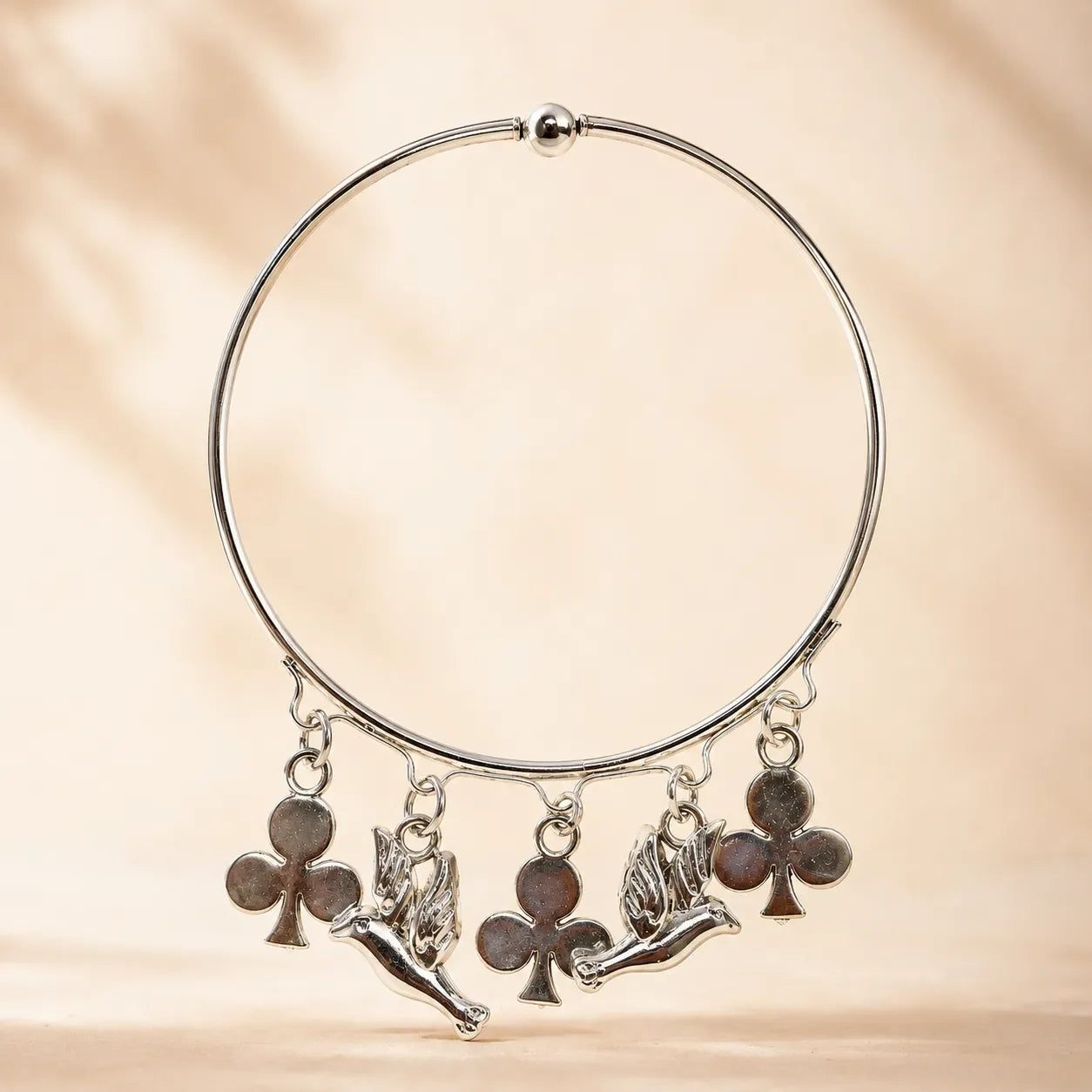 Side angle view of silver angel cherub and club charm bangle bracelet showing charm detail and ball bead top closure on warm background