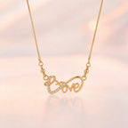 Gold Love script pendant necklace coiled on beige surface showing lobster clasp closure