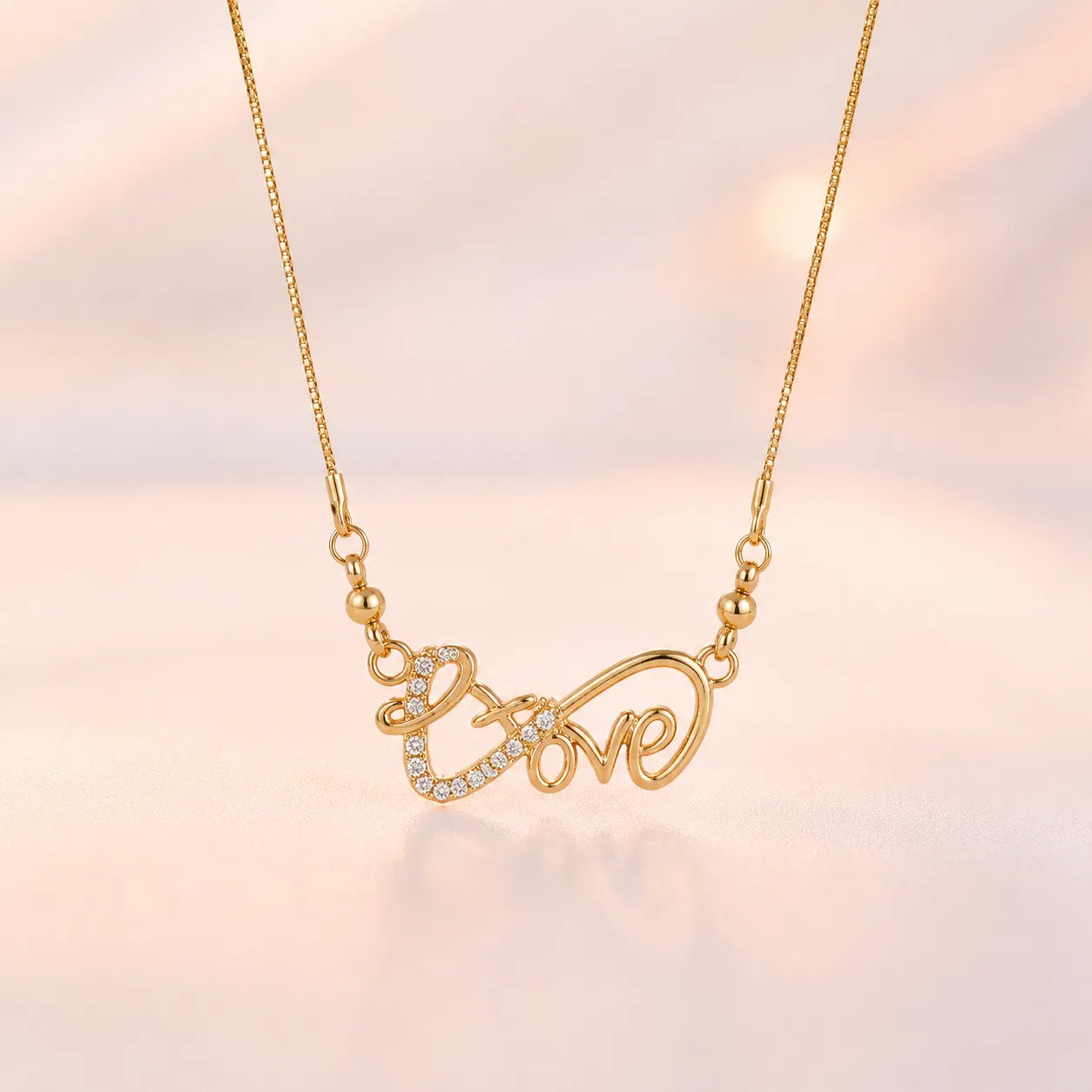 Gold Love script pendant necklace coiled on beige surface showing lobster clasp closure