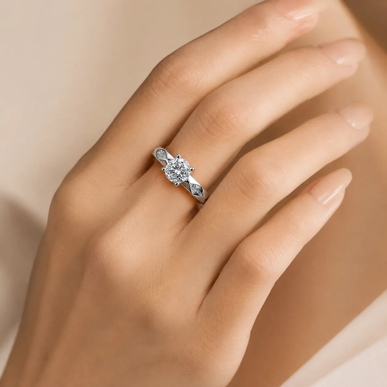 A silver engagement ring with a round center stone and small side stones, worn on a woman's hand against a soft beige background.