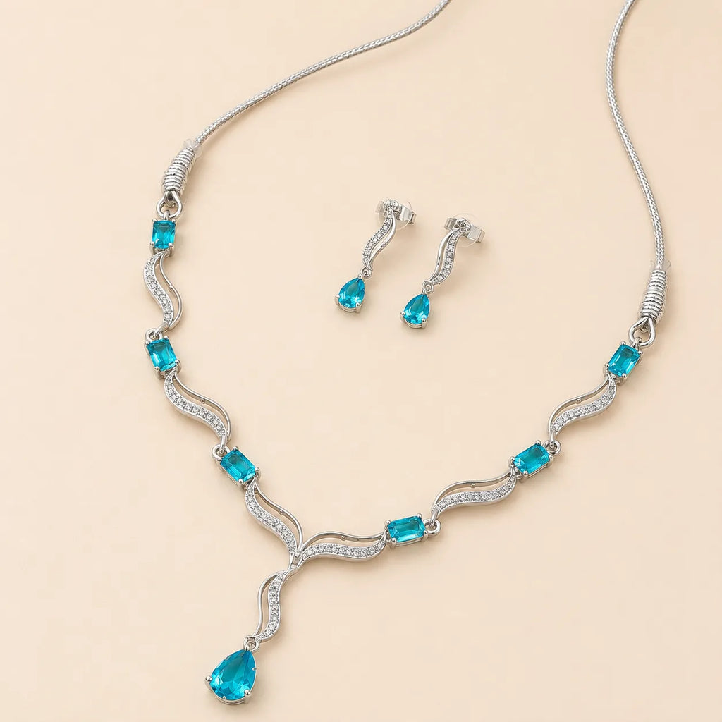 Blue crystal necklace and earring set laid flat showing teardrop pendant and wave-link chain