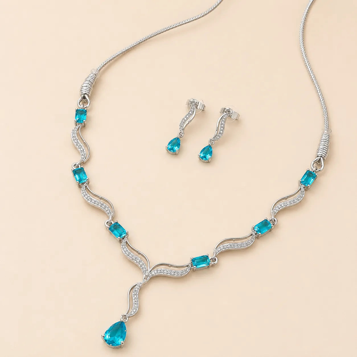 Blue crystal necklace and earring set laid flat showing teardrop pendant and wave-link chain