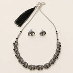 "Silver elephant necklace and earring set with black tassel on beige background"