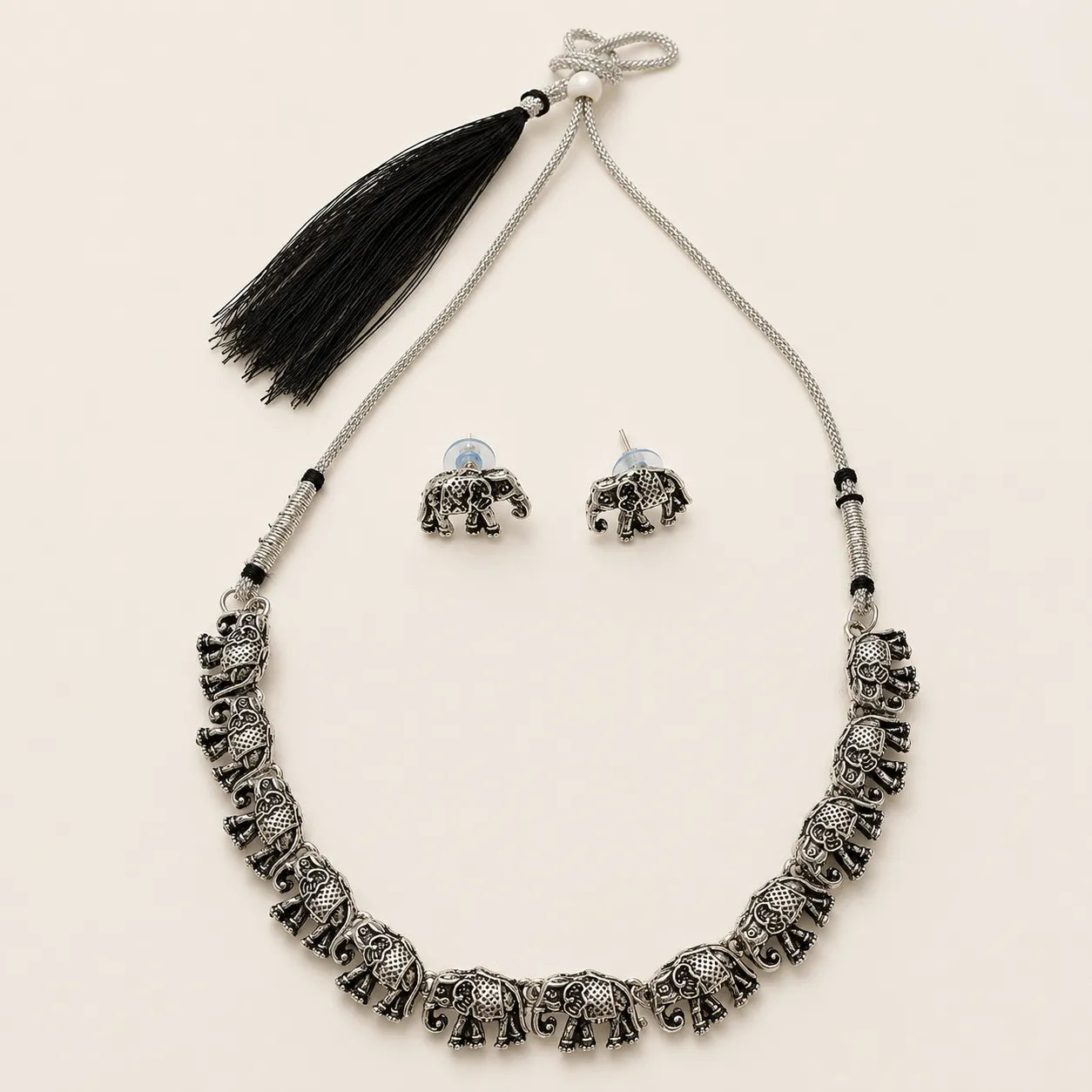 "Silver elephant necklace and earring set with black tassel on beige background"