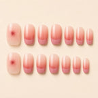 Set of 24 short square pink ombre French tip press-on nails with cherry blossom floral accent arranged in two rows on cream background